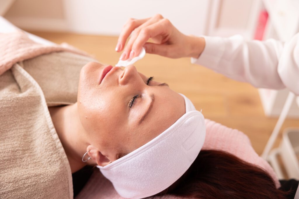 Eine Kundin liegt entspannt auf der Kosmetikliege in der Schönheitsmanufaktur Gilching und bekommt eine sanfte Gesichtsreinigung bevor die hochwirksame Gesichtsbehandlung mit Bio zertifizierten Naturkosmetikprodukten startet.