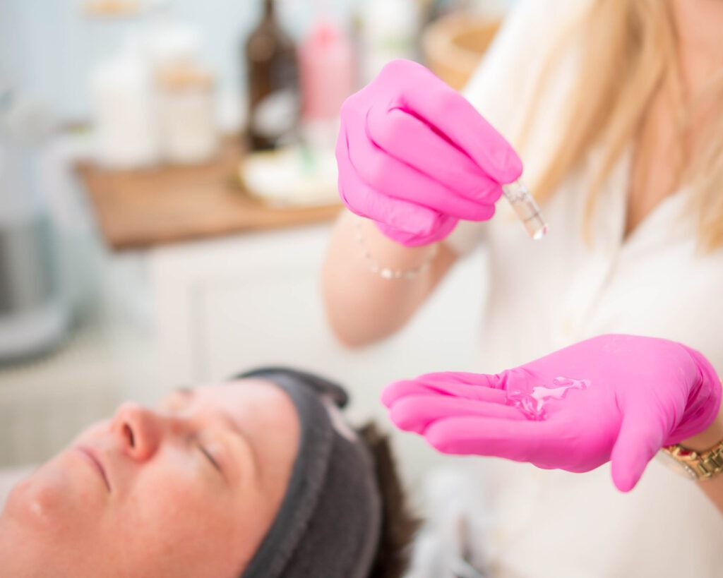 Kosmetikerin träufelt hochwirksame Bio zertifizierte Wirkstoff Serum auf einer Glasampulle bevor diese mit spezieller Technik in die Haut der Kundin eingearbeitet wird.